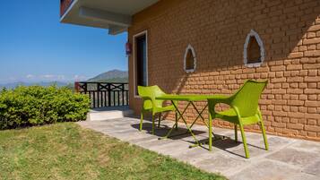 Un patio con dos sillas verdes y una mesa, un muro de ladrillo y vistas a las montañas.