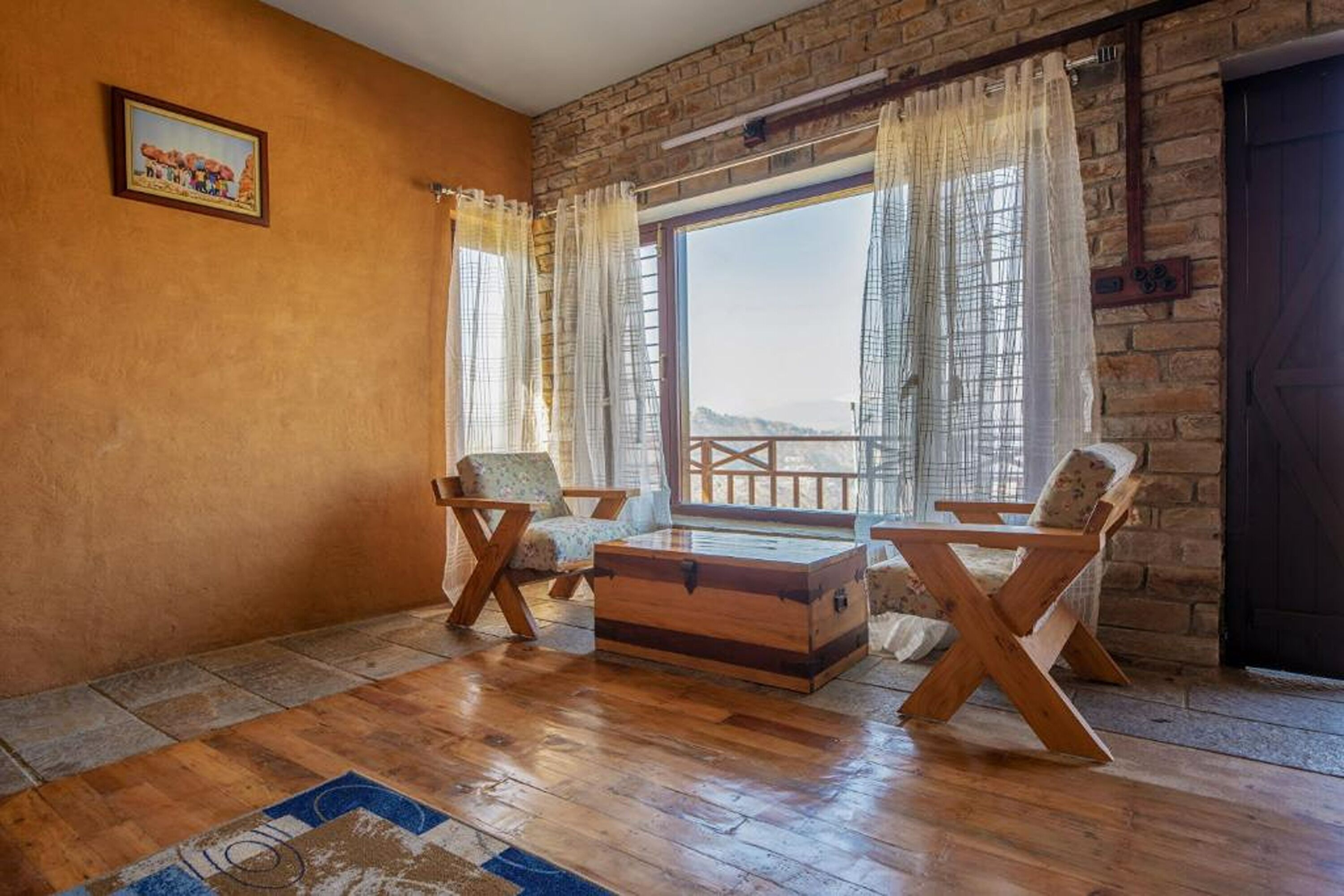 Une pièce chaleureuse avec un plancher en bois, deux chaises en bois, une commode en bois et une grande fenêtre avec des rideaux.