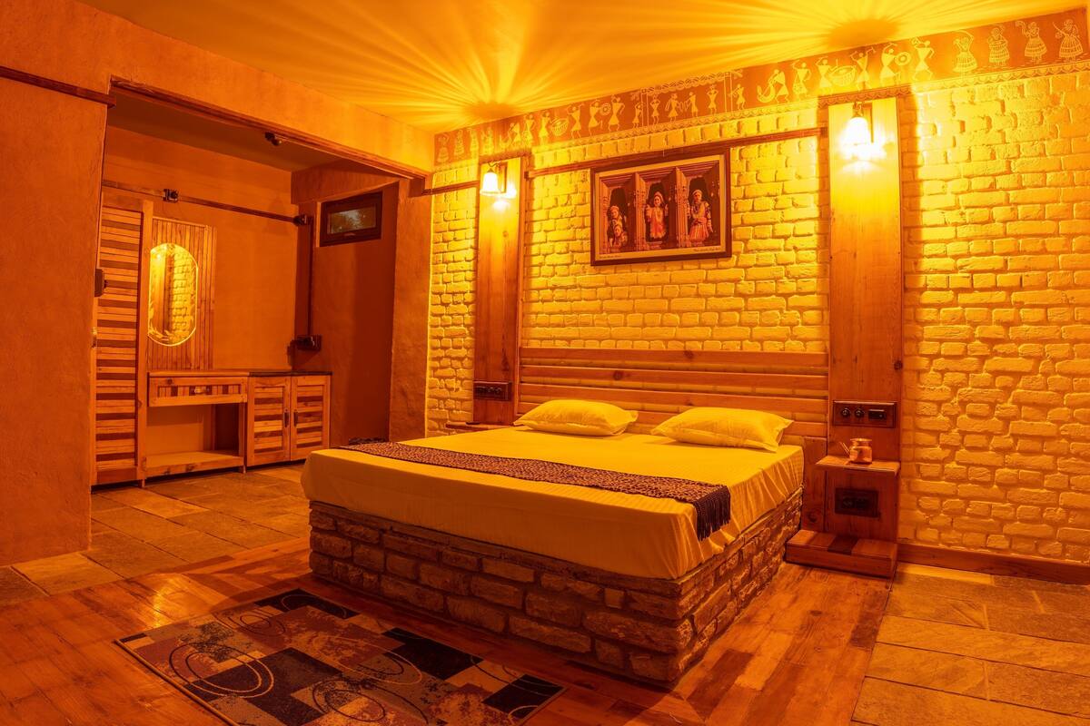 Een knus slaapkamer met een bakstenen muur, een bed met kussens, een nachtkastje en een houten garderobe.