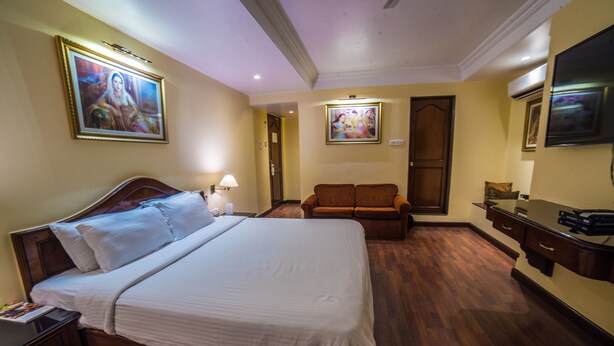 Una habitación de hotel con una cama grande, un aparador de madera, un televisor y dos cuadros en la pared.