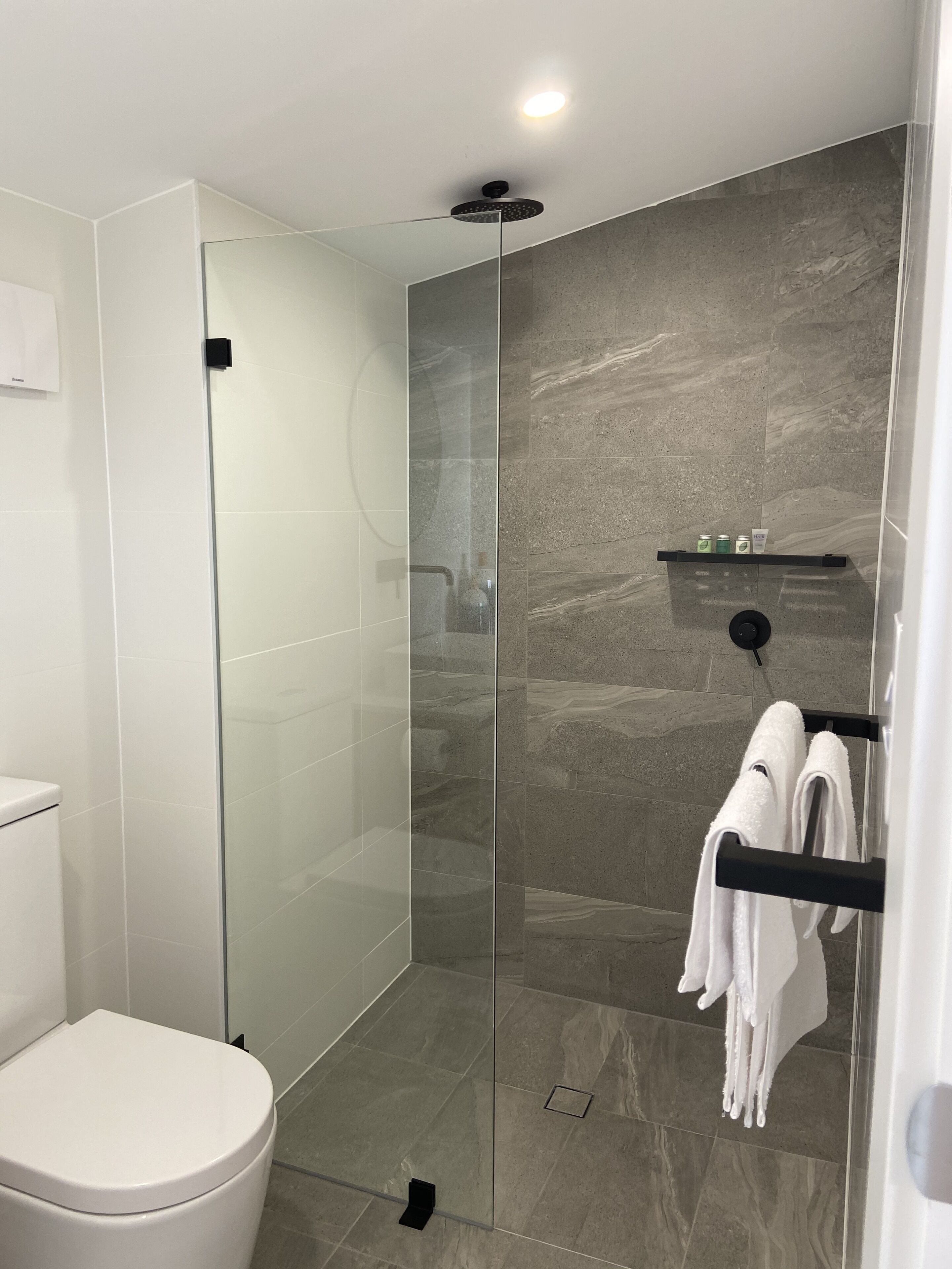 A modern bathroom with a glass-enclosed shower, a white toilet, and a towel rack with towels.
