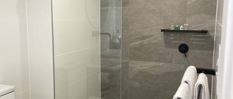 A modern bathroom with a glass-enclosed shower, a white toilet, and a towel rack with towels.