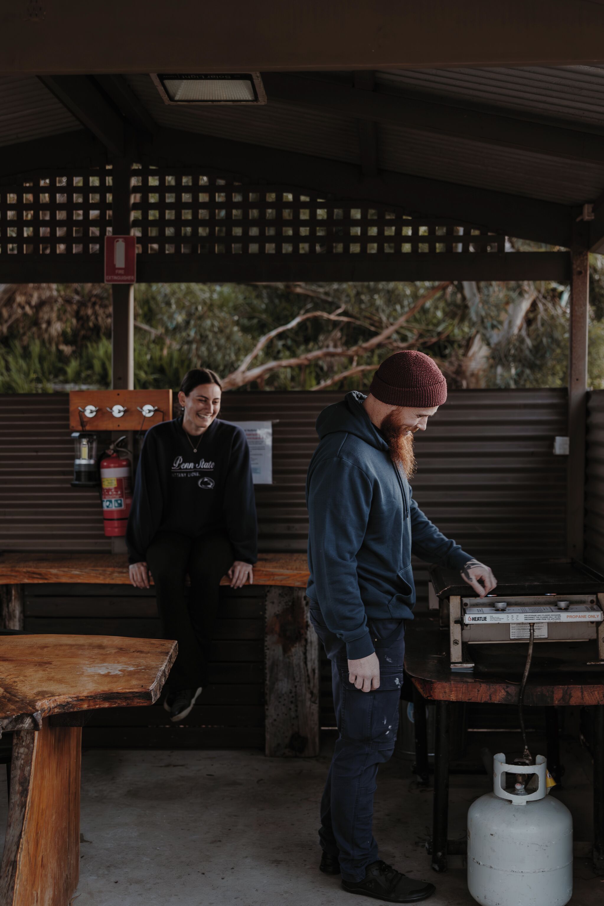 A covered outdoor area with a wooden bench, a gas stove, and a propane tank.