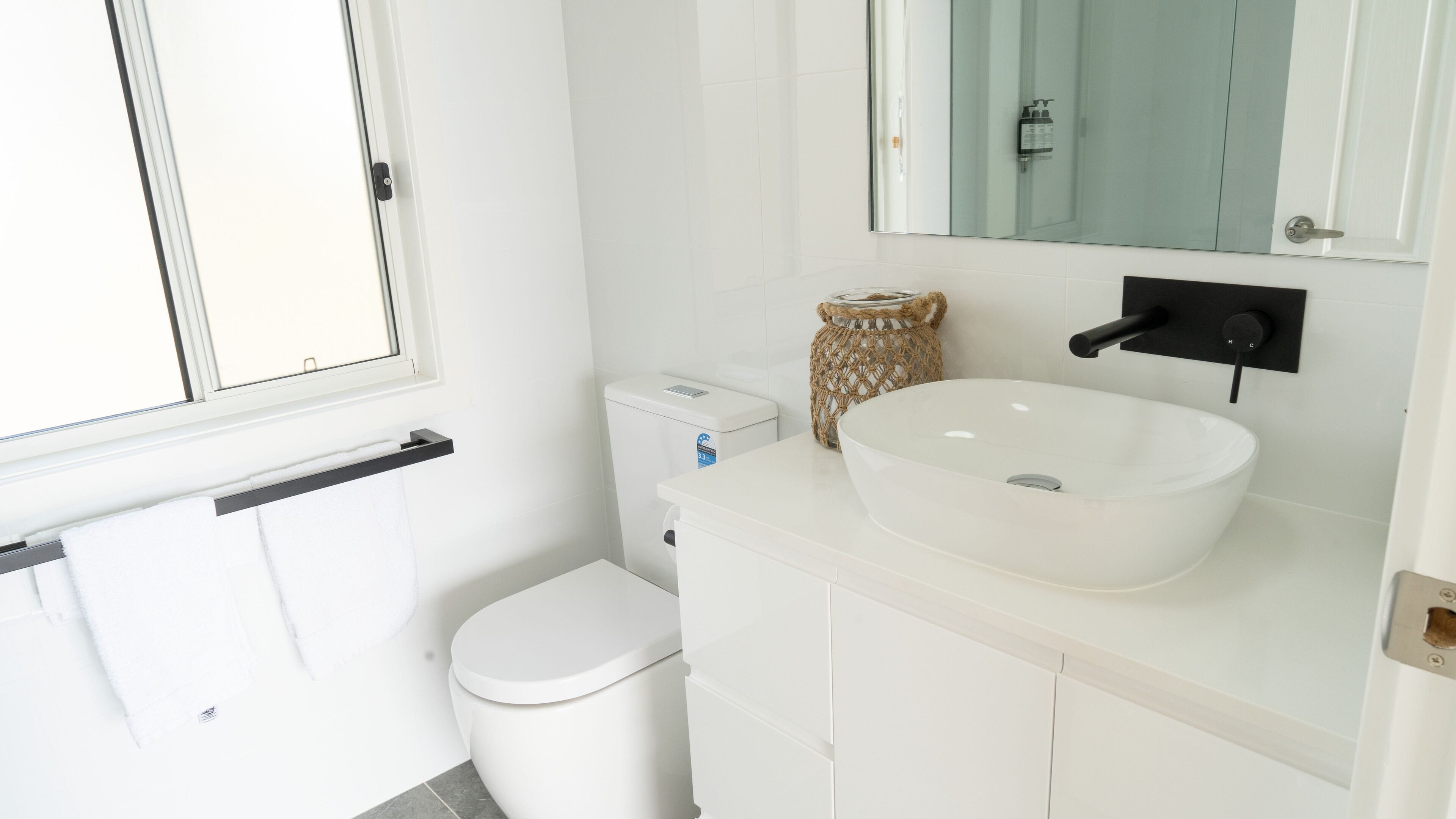 A modern bathroom with a white toilet, a white sink, and a mirror above the sink.