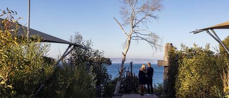 A pathway leading to a beach with a clear sky, a wooden fence, and a couple standing by the water.