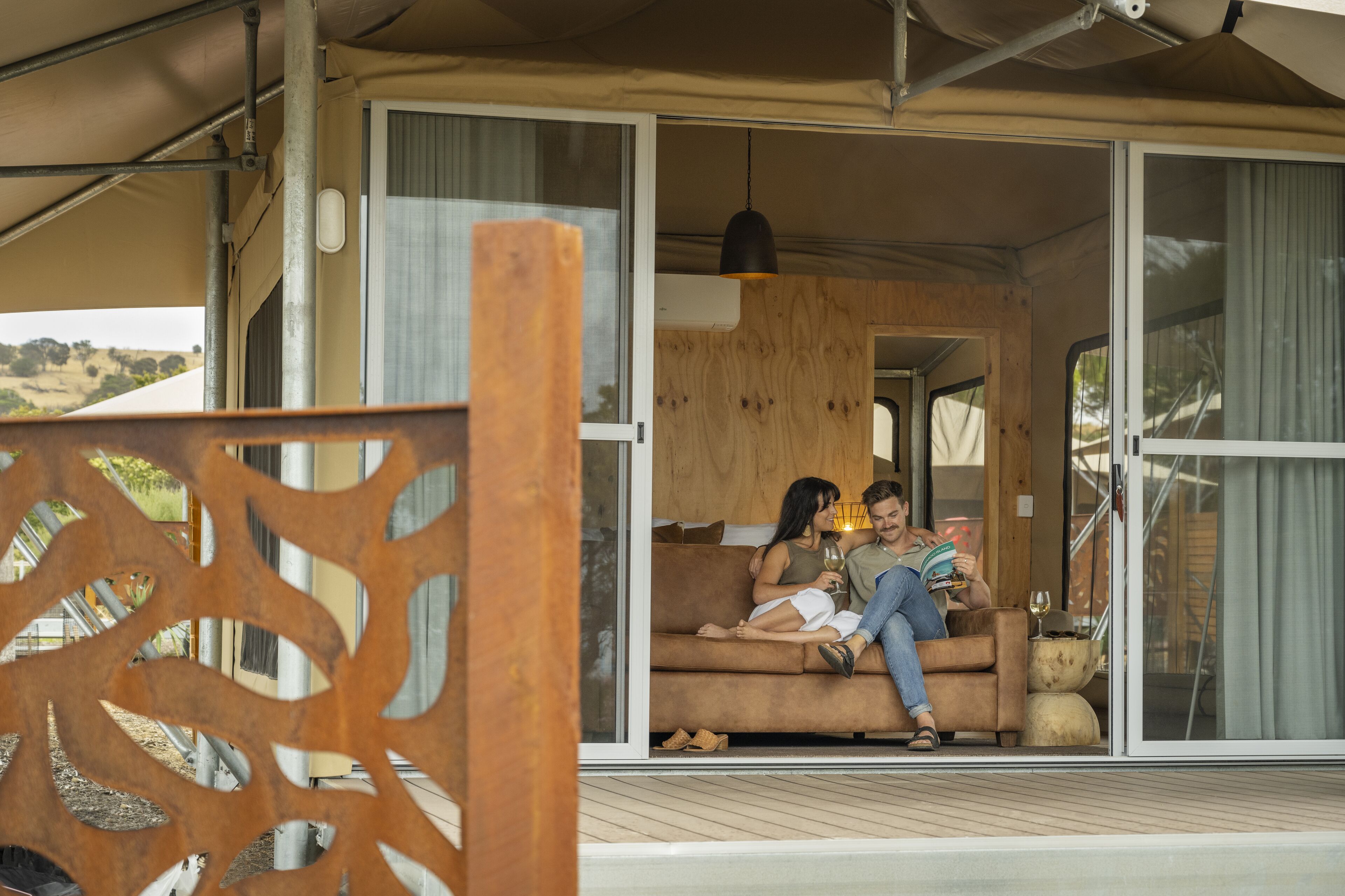 A couple sitting on a sofa in a room with large sliding glass doors, a wooden ceiling, and a hanging pendant light.