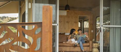 A couple sitting on a sofa in a room with large sliding glass doors, a wooden ceiling, and a hanging pendant light.