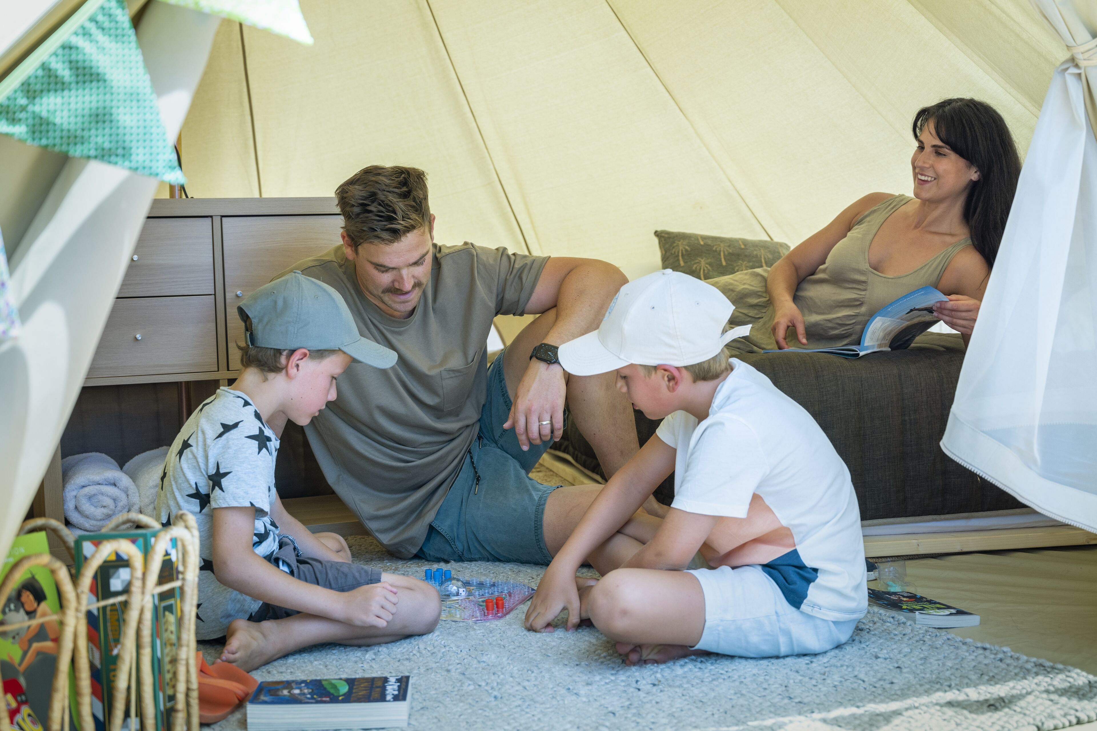 A family of four in a tented accommodation with a sleeping area, a small table, and a child's play area.