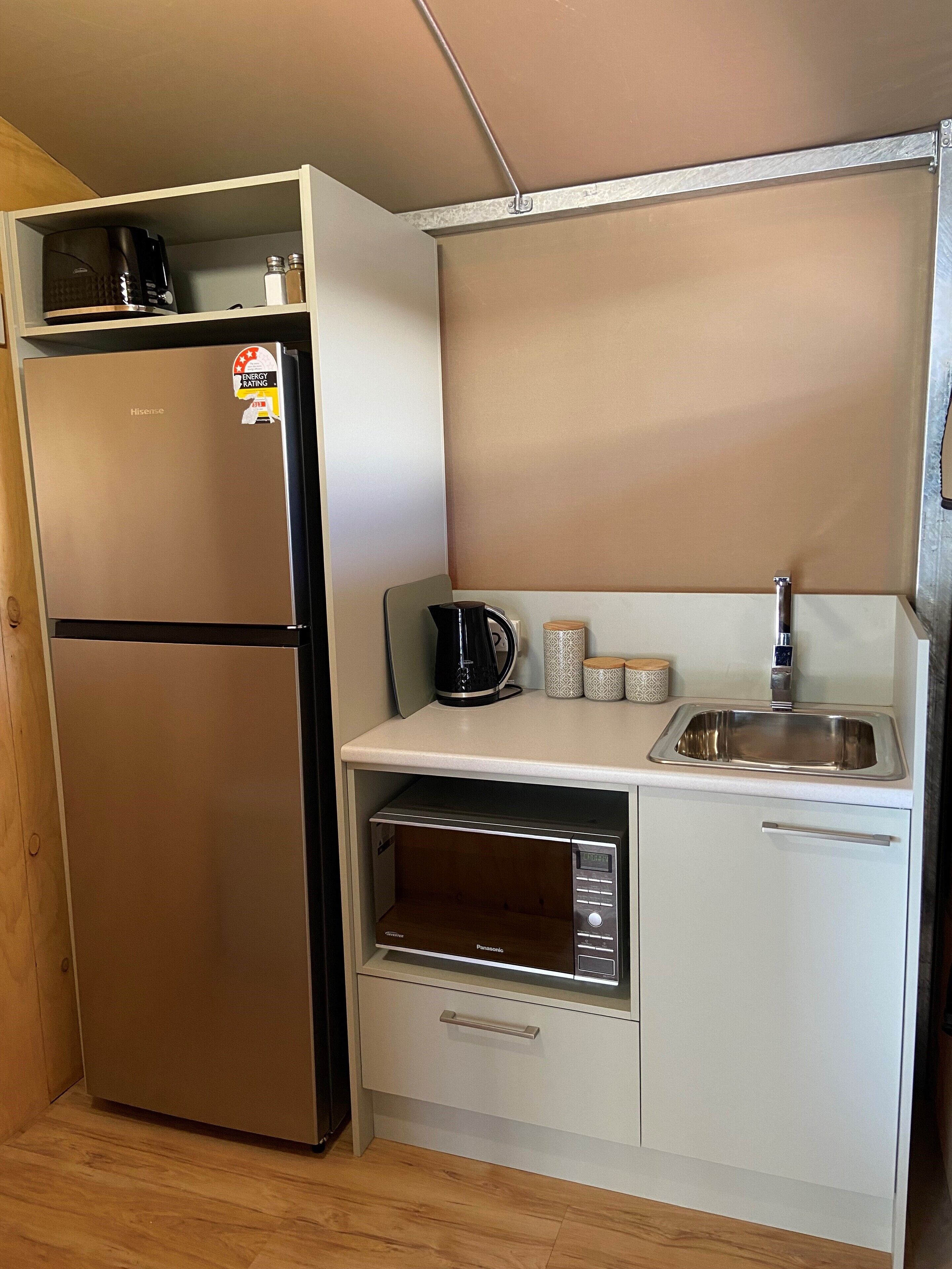 A compact kitchenette with a stainless steel refrigerator, a built-in oven, a sink, and a microwave.