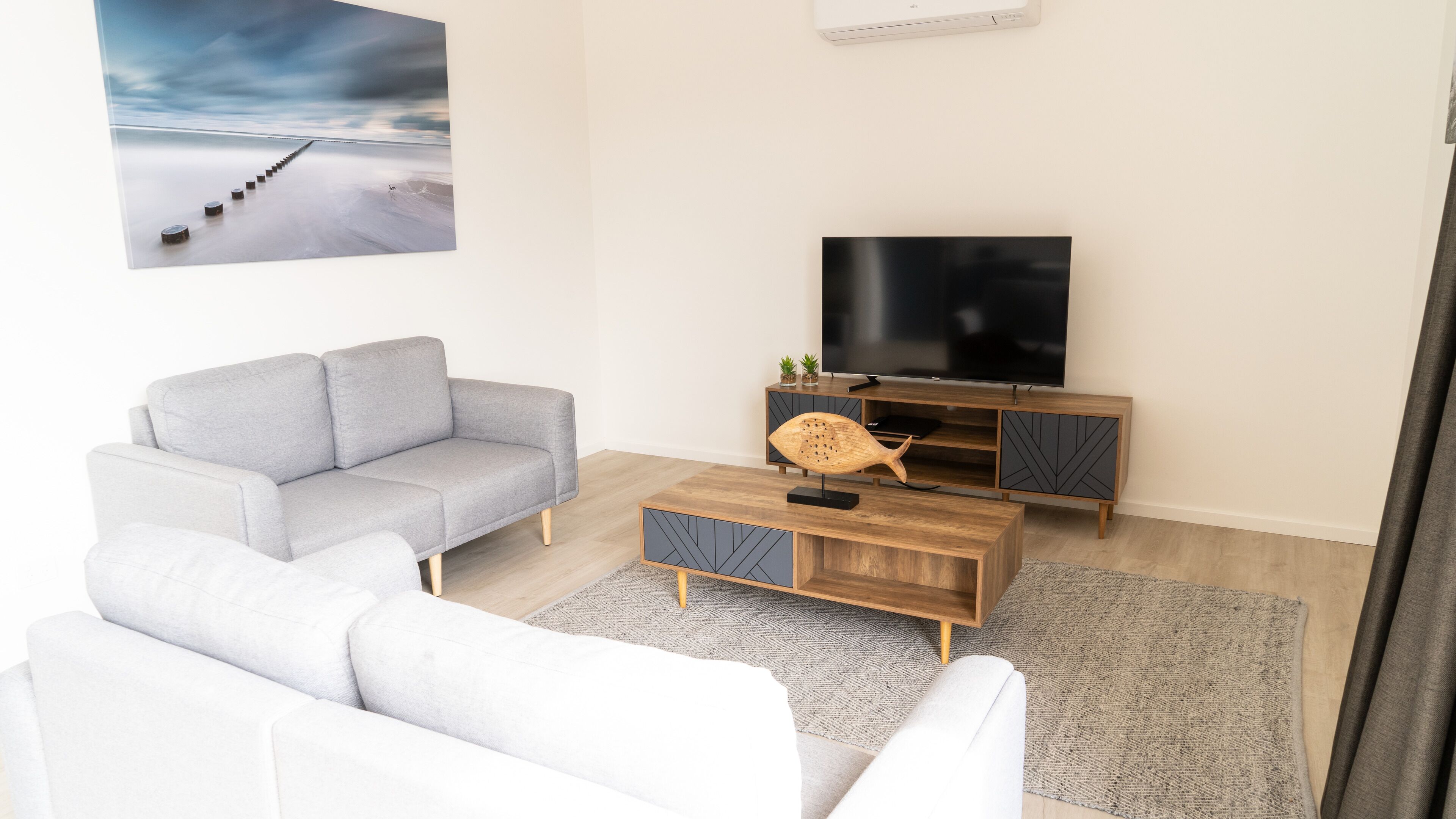 Una sala de estar moderna con un sofá gris, un sofá blanco, una mesa de centro de madera y un televisor sobre un mueble de madera.