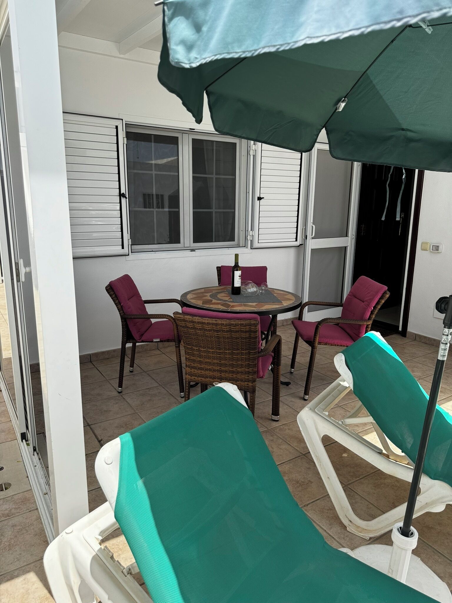 A patio area with a round table, four chairs, and a green umbrella.