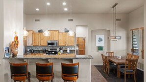 A modern kitchen with wooden cabinets, a granite countertop, and pendant lighting. There is a dining area with a wooden table and chairs. - Sprawling Arizona Oasis w/ Dream Backyard (New River)