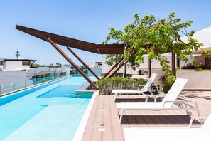 Una piscina en la azotea con sillones de descanso y una pérgola.