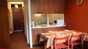 A compact kitchen with wooden cabinets, a microwave, and a dining area with a table and chairs.