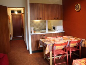 A compact kitchen with wooden cabinets, a microwave, and a dining area with a table and chairs.