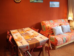Uma sala de jantar com uma mesa posta para quatro pessoas, um sofá e um relógio de parede.