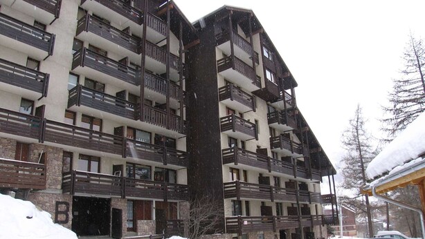 A multi-story building with balconies, a stone facade, and a snow-covered ground.