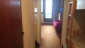 A narrow hallway with carpeted floors, a wooden door on the left, and a bunk bed on the right.