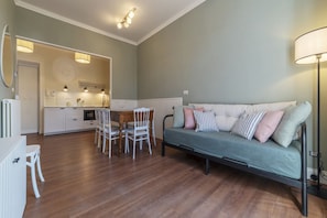 A modern living room with a sofa, dining table, chairs, and a kitchen area in the background.