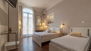 A hotel room with two beds, a desk, a chair, a mirror, and a window with curtains. - GuestHost - Comfortable and quiet 90sqm apartment that can accommodate up to 6 people. Located on the sixth floor, without lift (not suitable for the disabled, steps to access), of a renovated period building in Trastevere area, the apartment is located  (Roma)
