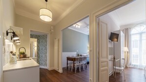 A hotel room with a wooden floor, a dining area with a table and chairs, a television mounted on the wall, and a large window with curtains. - GuestHost - Comfortable and quiet 90sqm apartment that can accommodate up to 6 people. Located on the sixth floor, without lift (not suitable for the disabled, steps to access), of a renovated period building in Trastevere area, the apartment is located  (Roma)