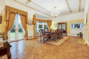A dining room with a wooden table and chairs, a chandelier, and large windows with curtains. - Blackpool Abode - Southlands (Blackpool)
