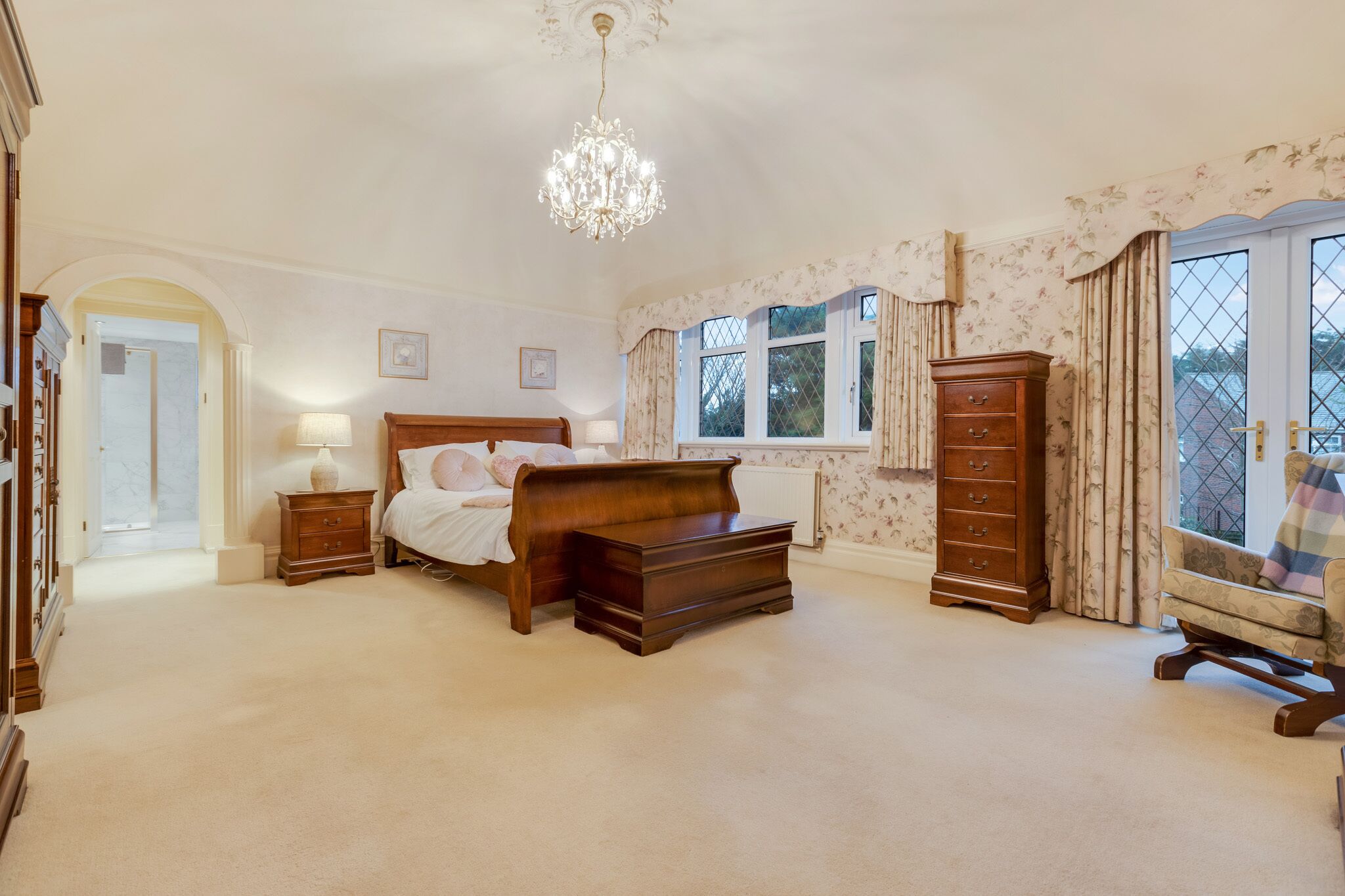 A bedroom with a large bed, a dresser, a nightstand, and a chair by the window.