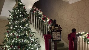 Eine imposante Treppe mit Weihnachtsbaum, geschmückt mit Lichtern und Dekorationen, führt zu einer Empore mit einem Kalender.