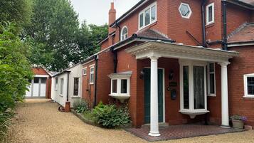 A red brick house with a white porch and a green door, surrounded by gravel and greenery.