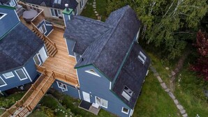 A multi-story house with a wooden deck, multiple windows, and a green roof. - Chouette Tremblant Ski In/Out Pedestrian Village (Mont-Tremblant)