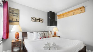A hotel room with a bed, two bedside tables with lamps, a wooden shelf with hooks, and a wall with three animal-themed pictures. - Chouette Tremblant Ski In/Out Pedestrian Village (Mont-Tremblant)