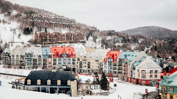 A snow-covered town with colorful buildings, a ski lift, and a mountain in the background. - Chouette Tremblant Ski In/Out Pedestrian Village (Mont-Tremblant)