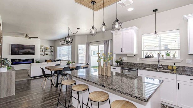 Una cocina moderna con una isla grande, taburetes de bar, iluminación colgante y un área de comedor con televisor.