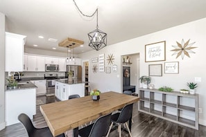 Una cocina moderna con armarios blancos, una mesa de comedor de madera y una lámpara colgante.