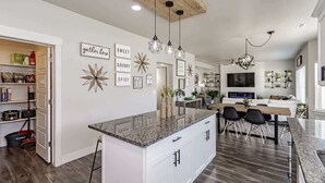 Una cocina moderna con una isla central, iluminación colgante y un comedor con sillas.