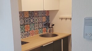 A small kitchen with a sink, a stove, and a microwave. There is a colorful tile backsplash and a white ceiling light.