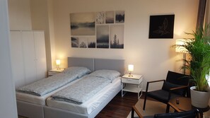 Un dormitorio con cama, dos mesitas de noche, una silla, una planta en maceta y decoración en la pared.