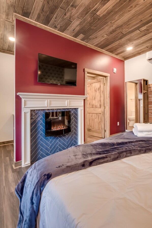 A bedroom with a fireplace, a bed, and a television mounted on the wall.