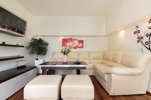 A modern living room with a beige sofa, a dining table with a vase of flowers, and a large potted plant.