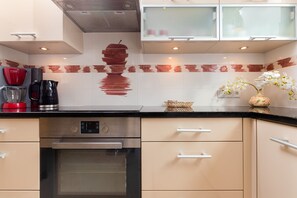 A modern kitchen with stainless steel appliances, beige cabinetry, and a decorative backsplash.