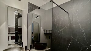 Un baño moderno con un espejo grande, un lavabo tipo cuenco y una pared de mármol negro.