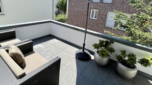 Terraza en la azotea con mobiliario exterior, una sombrilla grande y plantas en macetas.