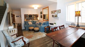 Una sala de estar acogedora con un sofá, otomanas, una mesa de comedor y una cocina al fondo.