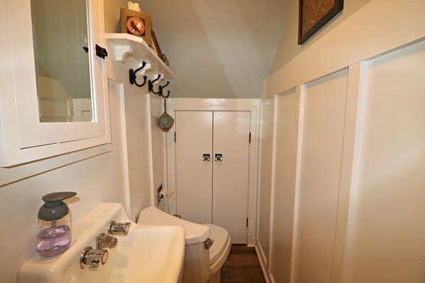 A bathroom with a toilet, sink, and a shower area. There is a shelf above the sink with decorative items.