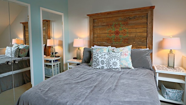 Un dormitorio con una cama grande, dos mesitas de noche con lámparas, un cabecero de madera con detalles decorativos y un espejo en la pared.