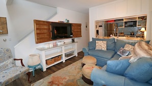 Una sala de estar con sofá, televisión y cocina al fondo.
