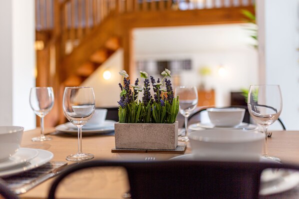 Una mesa de comedor con un centro de flores de lavanda, copas de vino transparentes y platos blancos.