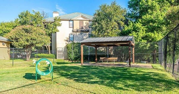 A fenced backyard with a wooden gazebo, a green play structure, and a house in the background.