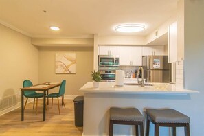 A modern kitchen with white cabinets, a central island, and a dining area with a table and chairs.