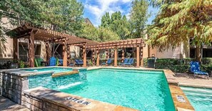 A swimming pool with a wooden pergola and lounge chairs.